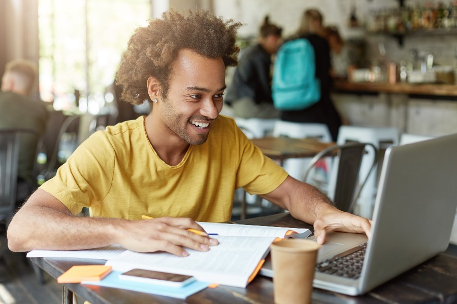 homem usando o notebook e segurando um livro aberto para definir o que estudar para o vestibular