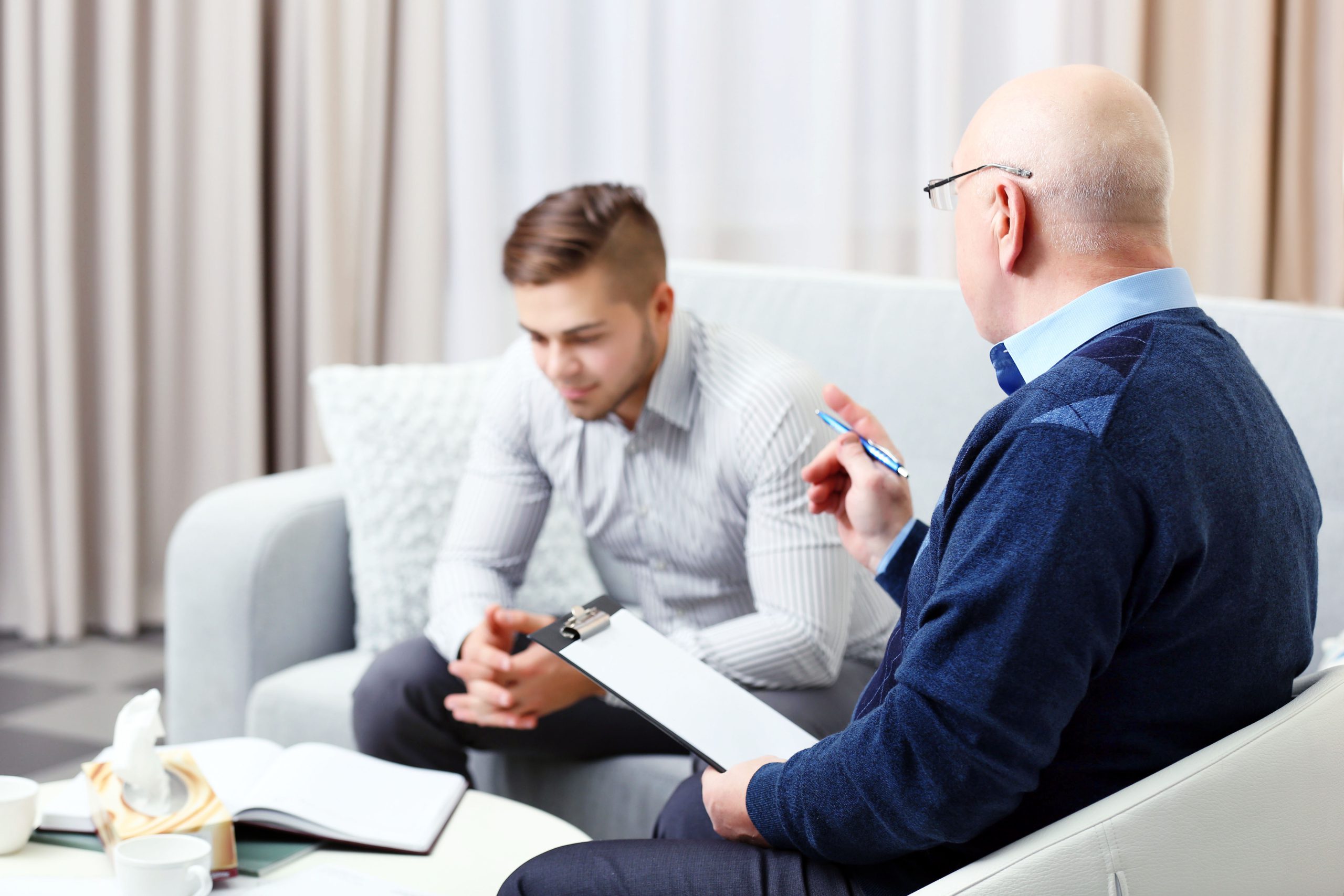 Jovem no consultório com psicólogo mais velho com sucesso profissional realizando anotações. 